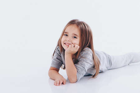 a little girl lying on the floor on a white background. Child promotes childrens clothesの写真素材