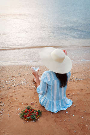 Diet. Healthy eating and rest. woman drinks clean water in glass background sea and eats strawberries. A woman on the beach enjoys lifeの写真素材