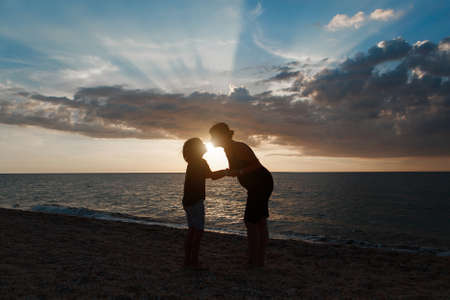 family on the beach. Silhouettes of people against the sunset. 2 people holding handsの写真素材