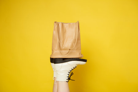 White womens shoes hold a beige bag on a yellow isolated background. Fashionable idea for discounts in stores and salons.の写真素材