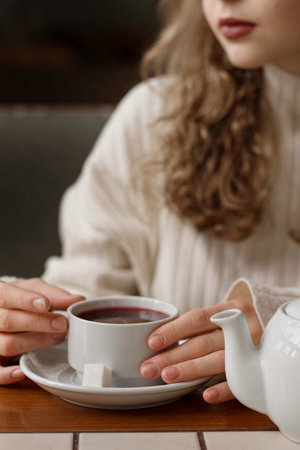 White blonde girl in a warm sweater drinks tea in a coffee shop. In a cafe, coffee is poured into a...
