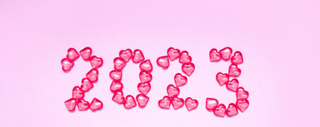 New Year 2023 inscription from glass hearts on a pink background. color 2023. Idea and creativity. Valentines Day. Christmas with loved ones. Horizontally, banner. High quality photoの写真素材