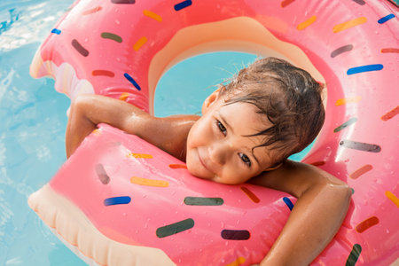 A European girl bathes in a blue pool in a pink large rubber ring. Wet hair and a happy smile. Waves, hotel and beach. The family is enjoying a happy vacation. High quality photo.の写真素材