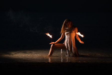 Caucasian woman in a white dress juggles with fireballs in the sea. Fire and water at night. Fire show on the waterfront. High quality FullHD footage. slow motion videoの写真素材
