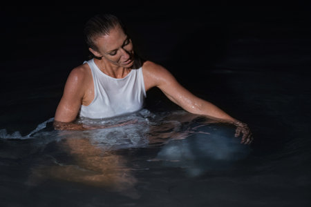 Caucasian woman in a white dress bathes in the night sea. The girl in the water in the evening poses beautifully at sunset on vacation. Relaxation, rest and enjoyment, meditation in the river.の写真素材