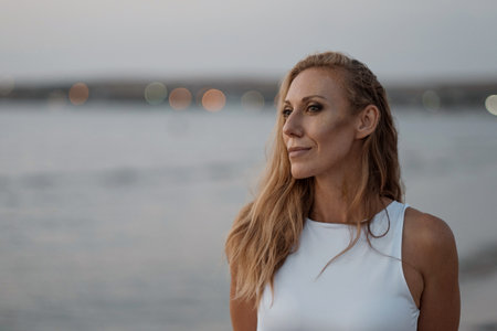 Caucasian woman with white curly hair smiles beautifully at sunset. Rest on the beach near the sea. Rest for mom. Athlete walks along the ocean. High quality FullHD footage.の写真素材