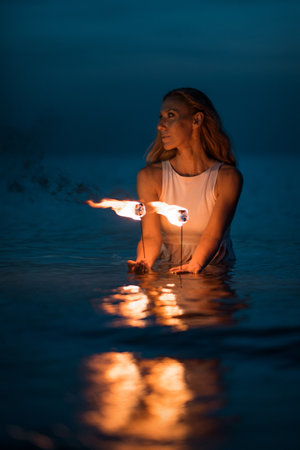 Caucasian woman dancing with fire in the water. Fire show at sea. Acrobatics on the beach. Yoga and relaxation at sunset. Spectacular circus performance. model body. High quality FullHD footage.の写真素材