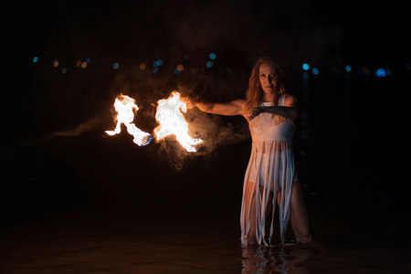 Caucasian woman dancing with fire in the water. Fire show at sea. Acrobatics on the beach. Yoga and relaxation at sunset. Spectacular circus performance. model body. High quality FullHD footage.の写真素材
