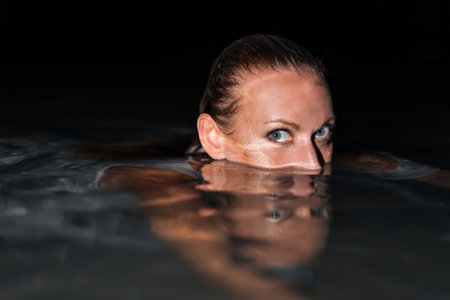 Caucasian woman in a white dress bathes in the night sea. The girl in the water in the evening poses beautifully at sunset on vacation. Relaxation, rest and enjoyment, meditation in the river.の写真素材