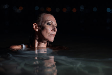Caucasian woman in a white dress bathes in the night sea. The girl in the water in the evening poses beautifully at sunset on vacation. Relaxation, rest and enjoyment, meditation in the river.の写真素材