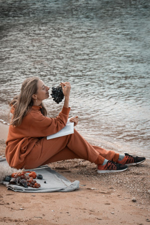 A girl in an orange tracksuit, hoodie and pants sits on the beach and enjoys. Sits by the sea and...