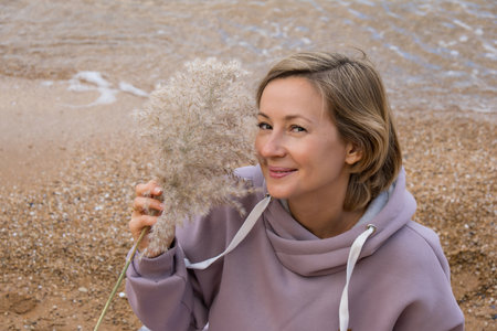 Portrait of a blonde girl with fair skin. A woman sits on the beach and reads a book, eats and relaxes, enjoys the moment. Self love, meditation on the ocean, rocks. High quality photoの写真素材