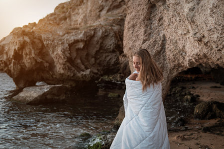 a girl in a white blanket walks along the beach at the sea, near the rocks. Beautiful, slender legs walk along the beach. Cream for varicose veins. High quality photoの写真素材