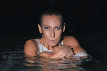 Caucasian woman in a white dress bathes in the night sea. The girl in the water in the evening poses beautifully at sunset on vacation. Relaxation, rest and enjoyment, meditation in the river.の写真素材
