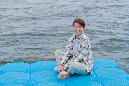 A tourist girl sits on a blue pier and enjoys the wind and sun, relaxation. High quality photo
