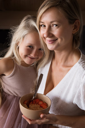 mother and daughter blonde with long hair hug and kiss each other. Mothers love, tenderness and care. The daughter is offended and sad, offended. Woman comforting a child at home. High quality photoの写真素材