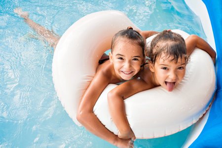 Two European girls, sisters girlfriends on an inflatable circle in the pool play, have fun, enjoy. Family holidays, the joy of holidays and fun on the beach at the hotel. High quality photo.の写真素材