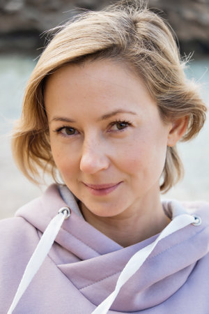 Portrait of a blonde girl with fair skin. A woman sits on the beach and reads a book, eats and relaxes, enjoys the moment. Self love, meditation on the ocean, rocks. High quality photoの写真素材