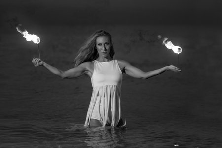 Caucasian woman in a white dress juggles with fireballs in the sea. Fire and water at night. Fire show on the waterfront. High quality FullHD footage. slow motion videoの写真素材