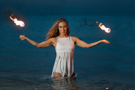 Caucasian woman in a white dress juggles with fireballs in the sea. Fire and water at night. Fire show on the waterfront. High quality FullHD footage. slow motion videoの写真素材