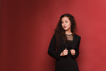 fashion female portrait. Girl, curly girl with black hair in a strict business suit on a red, pink background. High quality photoの写真素材