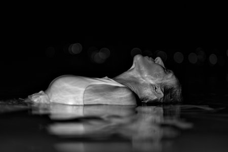 Caucasian woman in a white dress bathes in the night sea. The girl in the water in the evening poses beautifully at sunset on vacation. Relaxation, rest and enjoyment, meditation in the river.の写真素材