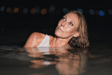 Caucasian woman in a white dress bathes in the night sea. The girl in the water in the evening poses beautifully at sunset on vacation. Relaxation, rest and enjoyment, meditation in the river.の写真素材