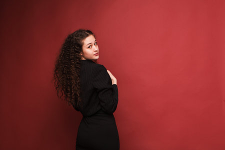 fashion female portrait. Girl, curly girl with black hair in a strict business suit on a red, pink background. High quality photoの写真素材