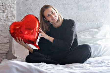 a girl with red heart-shaped balloons smiles and enjoys life. Caucasian woman celebrating valentines day. A note to your boyfriend. The concept of human emotions, facial expressions, relationships, romantic holidays. High quality photoの写真素材
