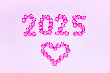 New Year 2025 inscription from glass hearts on a pink background. Pantone color 2025. Idea and creativity. Valentines Day. Christmas with loved ones. Horizontally, banner.の写真素材