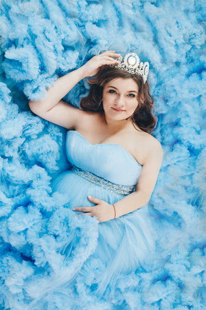 pregnant girl lies on a blue background. girl in a blue dress. girl with a diamond crownの写真素材