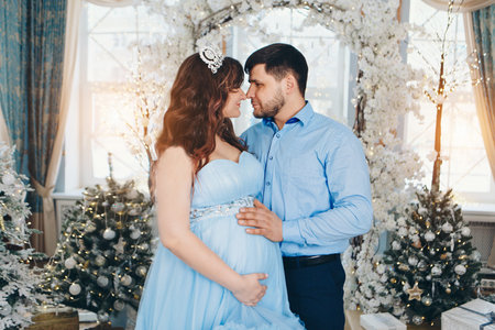 man and woman bowed their heads to each other. a young pregnant girl in a lush festive blue dress and a young man in a blue shirt. man put his hand on pregnant womans belly.の写真素材