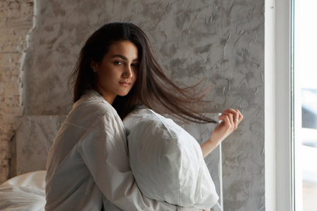 A woman with black hair wakes up in the morning in a white blanket. The portrait is creative, with brown eyes.の写真素材