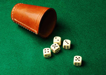 Five dices and a leather cup on green cloth