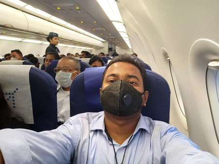 Sick man wear face mask sitting on passenger economy seat near cabin window in airplane. Passenger in departure flight plane at the airport. Novel coronavirus (2019-nCoV) infection or Wuhan coronavirus.のeditorial素材
