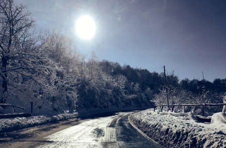 Beautiful winter road view between snow covered trees and sun on the top