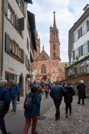 Basel, Switzerland - December 10, 2025: The Basel Minster rises above the Rhine with its red sandstone Gothic architecture and colorful roof as visitors gather at the historic site.のeditorial素材