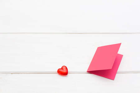 small red heart with the pink card on the white wooden background. festive background for Valentine's day, birthday, holiday, partyの写真素材