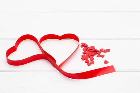 a lot of little red hearts and a red ribbon in the form of heart on white wooden background....
