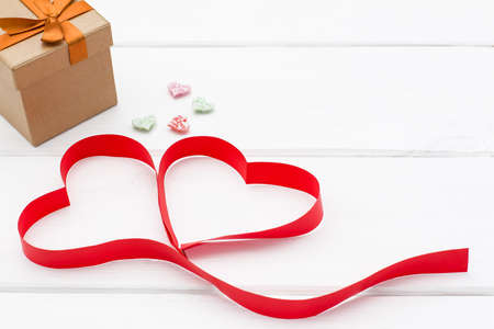 heart made of red ribbon, a few little hearts and gift box on white wooden background. valentines day concept. romantic love background for birthday, holiday, party, weddingの写真素材