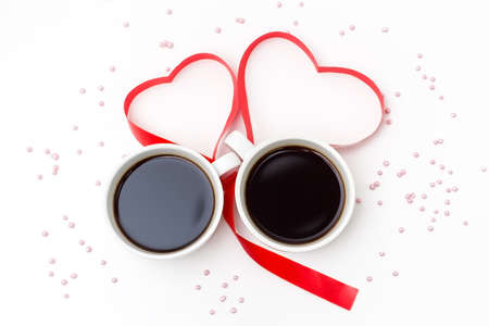 Cup of black coffee and a red ribbon in the shape of hearts on a white background with pink...