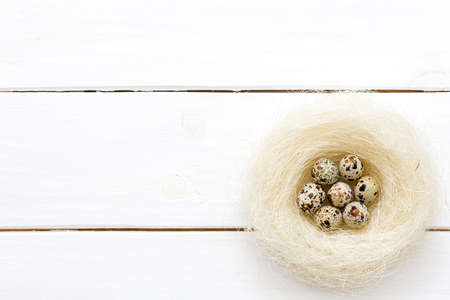 Easter quail eggs in nest on white wooden background.Top view.