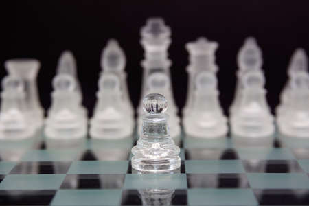 Glass chess on a black background. One pawn against the opponent's pieces. Business concept.の写真素材