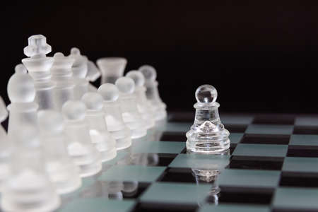 One pawn in front of the opponent's pieces. Minimal business concept. Glass chess on a black background.の写真素材