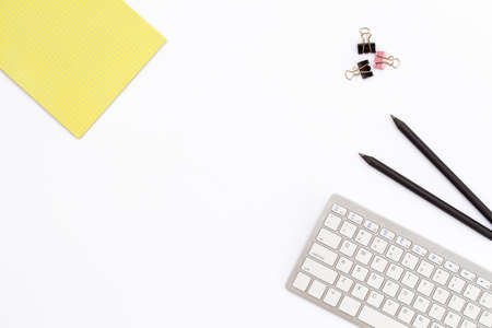 Yellow Notepad, computer keyboard, two black pencil and clips for paper on white background. minimal concept of desktop in the office. Flat lay. Top view.の写真素材