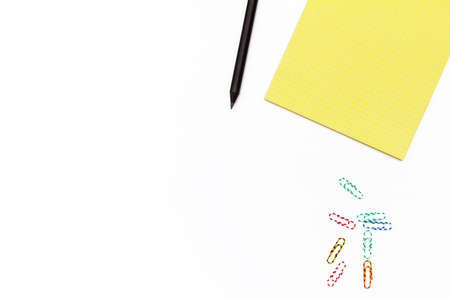 Yellow Notepad, black pencil, and colored paper clips on a white background. Minimal business...