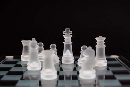 The king is surrounded by other figures. Glass Chess on a black background. Minimum business...
