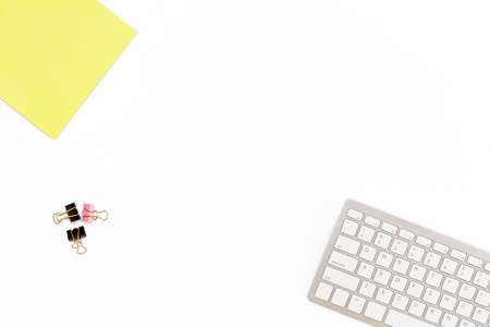 yellow Notepad, computer keyboard and clips for paper on white background. Minimal business concept for desktop in the office. Flat lay. Top view.の写真素材