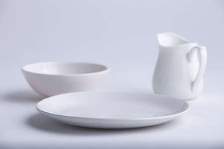 White Table wares,different shapes of an empty white ceramic plate,bowl and teapot arranged on a white textured background.の写真素材