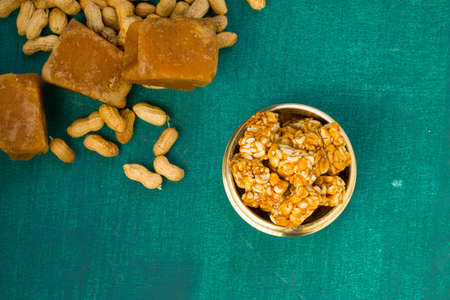 Peanut bar,crunchy sweet peanut bar which is very healthy and tasty snack,arranged in a brass vessel with peanut and jaggery on the dark green colour  background,selective focus.の写真素材